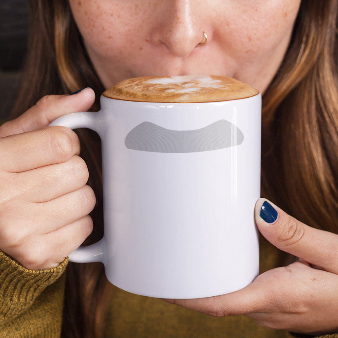 Woman holding a white ceramic mug with a drawing of Albert Einstein’s mustache, set against a plain white background.