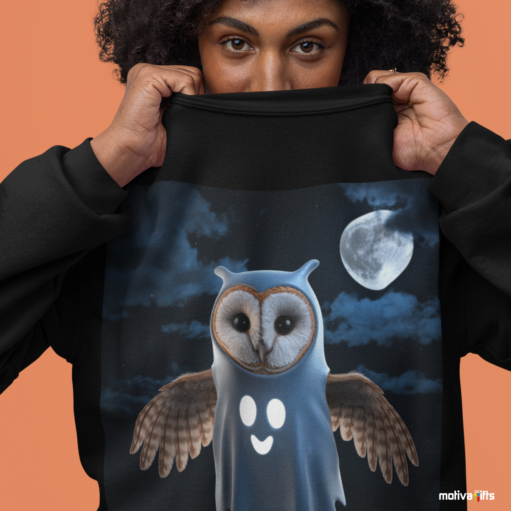 Woman wearing a black sweatshirt featuring a design of a barn owl dressed in a ghost Halloween costume