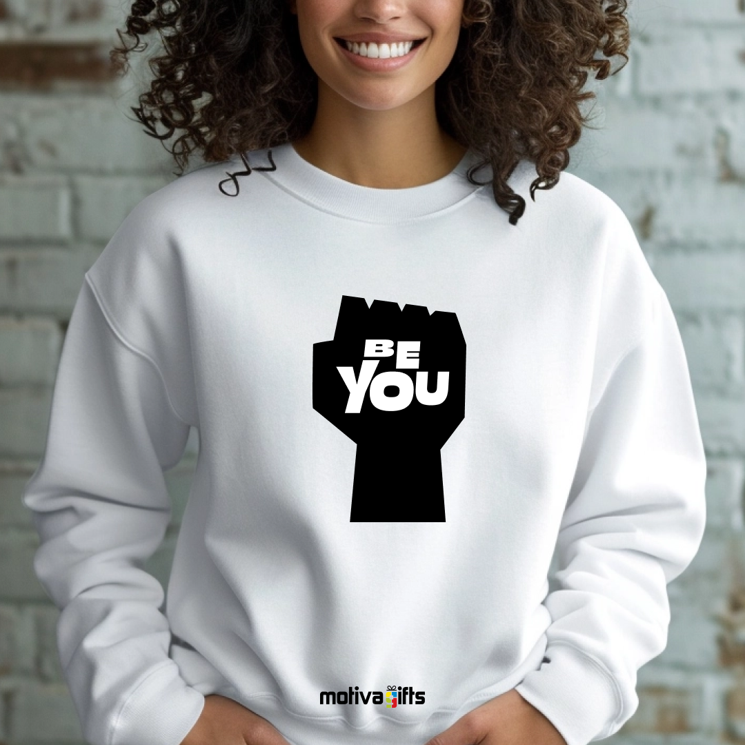 A woman wearing a white sweatshirt featuring bold black typography that reads Be You 