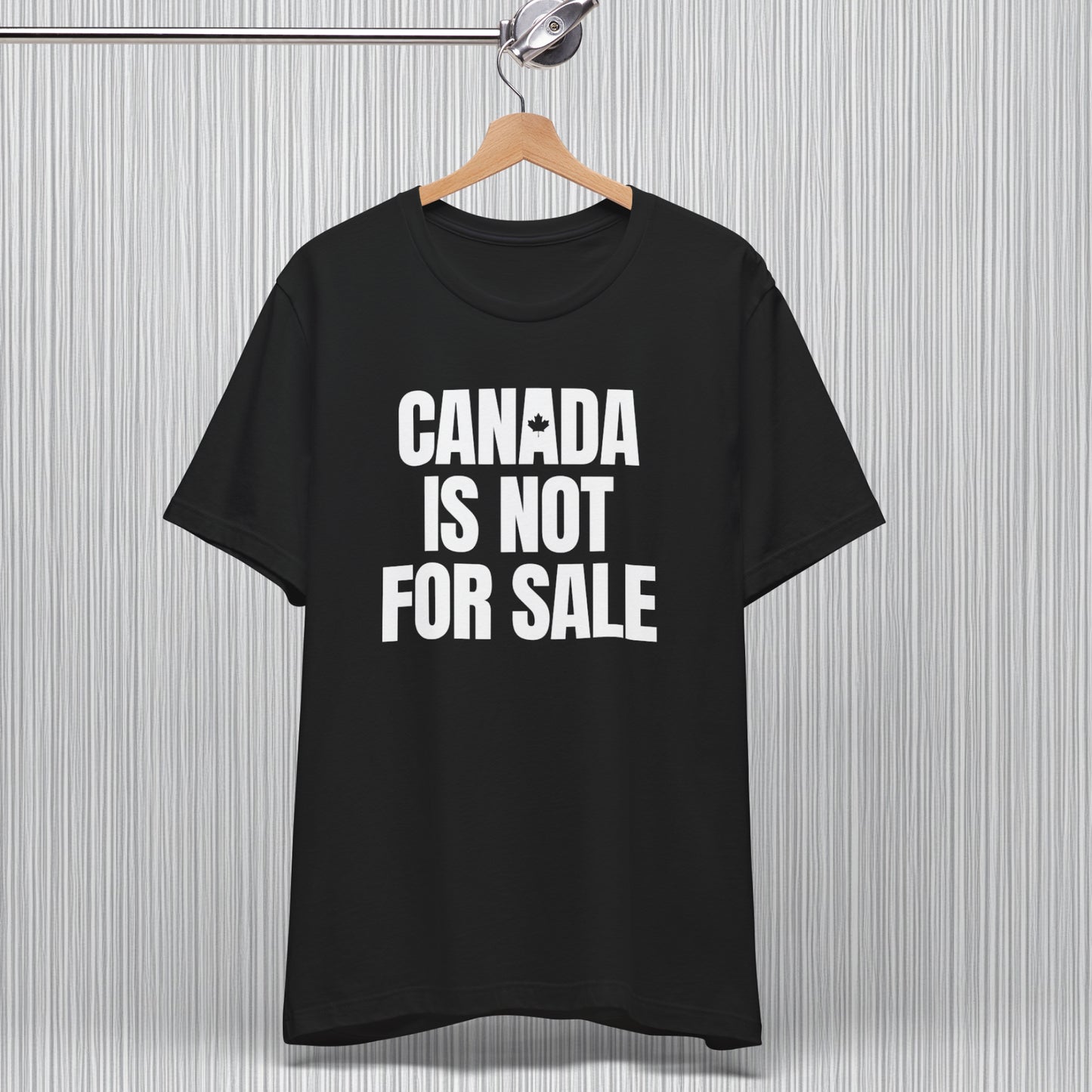 A hanging black T-shirt featuring bold white typography that reads 'Canada is Not for Sale