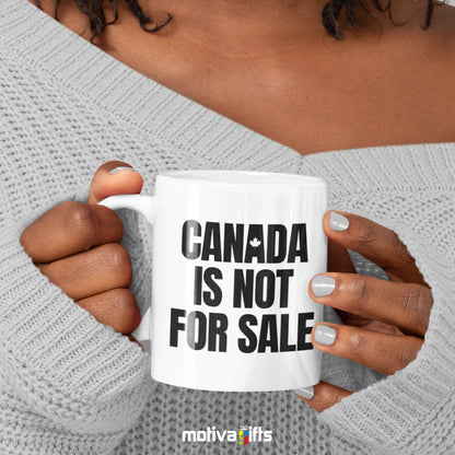 A woman holding a white 11oz ceramic mug featuring Canada is Not For Sale art printed on both sides