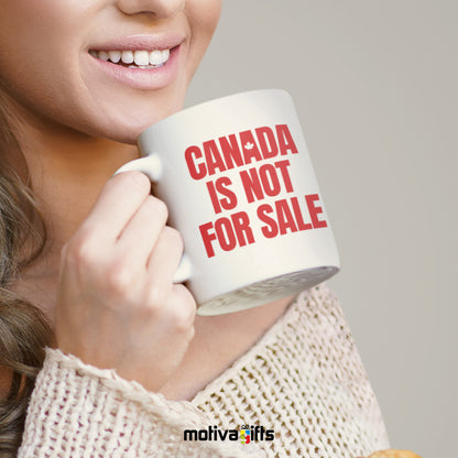 A woman holding a white 11oz ceramic mug that reads in Red bold Canada is Not For Sale art printed on both sides