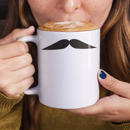 Woman holding a white ceramic mug with a drawing of Clark Gable’s mustache, set against a plain white background.