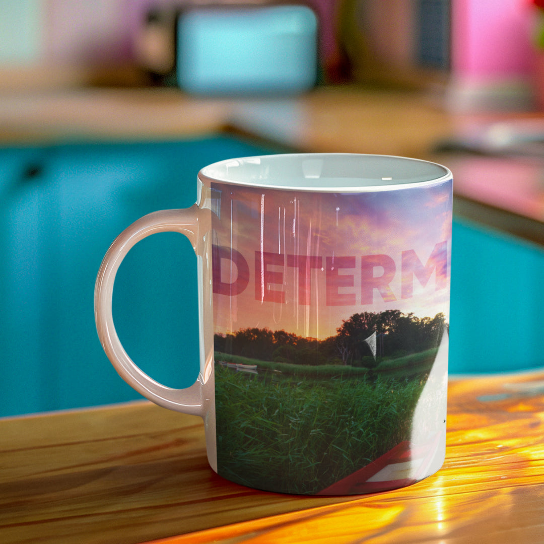 White ceramic mug with a wraparound art design featuring the word ‘Determination’ above a quote by Woman holding a white ceramic mug with a wraparound design displaying the word ‘Determination’ above a quote by Confucius: ‘Wherever you go, go with all your heart’, placed on a rustic table.