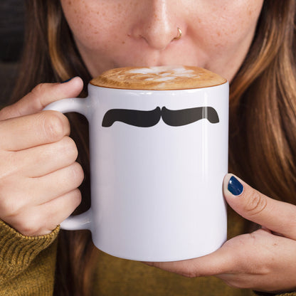 Woman holding a white ceramic mug with a drawing of Freddie Mercury’s mustache, set against a plain white background.