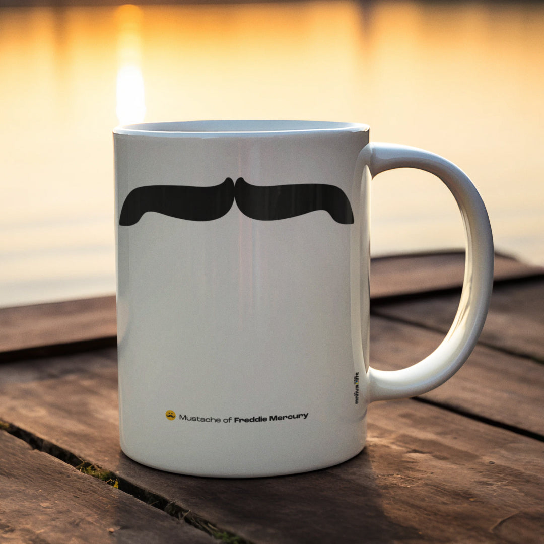 White ceramic mug with a drawing of Freddie Mercury’s mustache placed in front of a lake at sunrise 