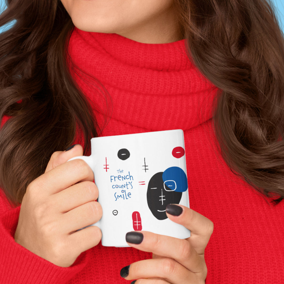 Woman holding a white ceramic mug with a drawing of The French Count’s Smile Mug