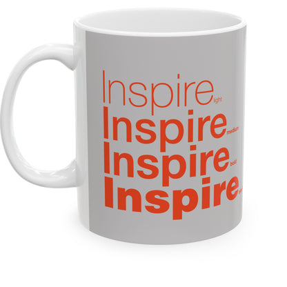 white ceramic mug with a grey wraparound design and the word 'Inspire' printed in red in four typography styles: light, medium, bold, and black. Clean white background.