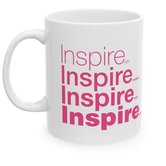 White ceramic mug with a white wraparound design and the word 'Inspire' printed in pink in four typography styles: light, medium, bold, and black. Clean white background.