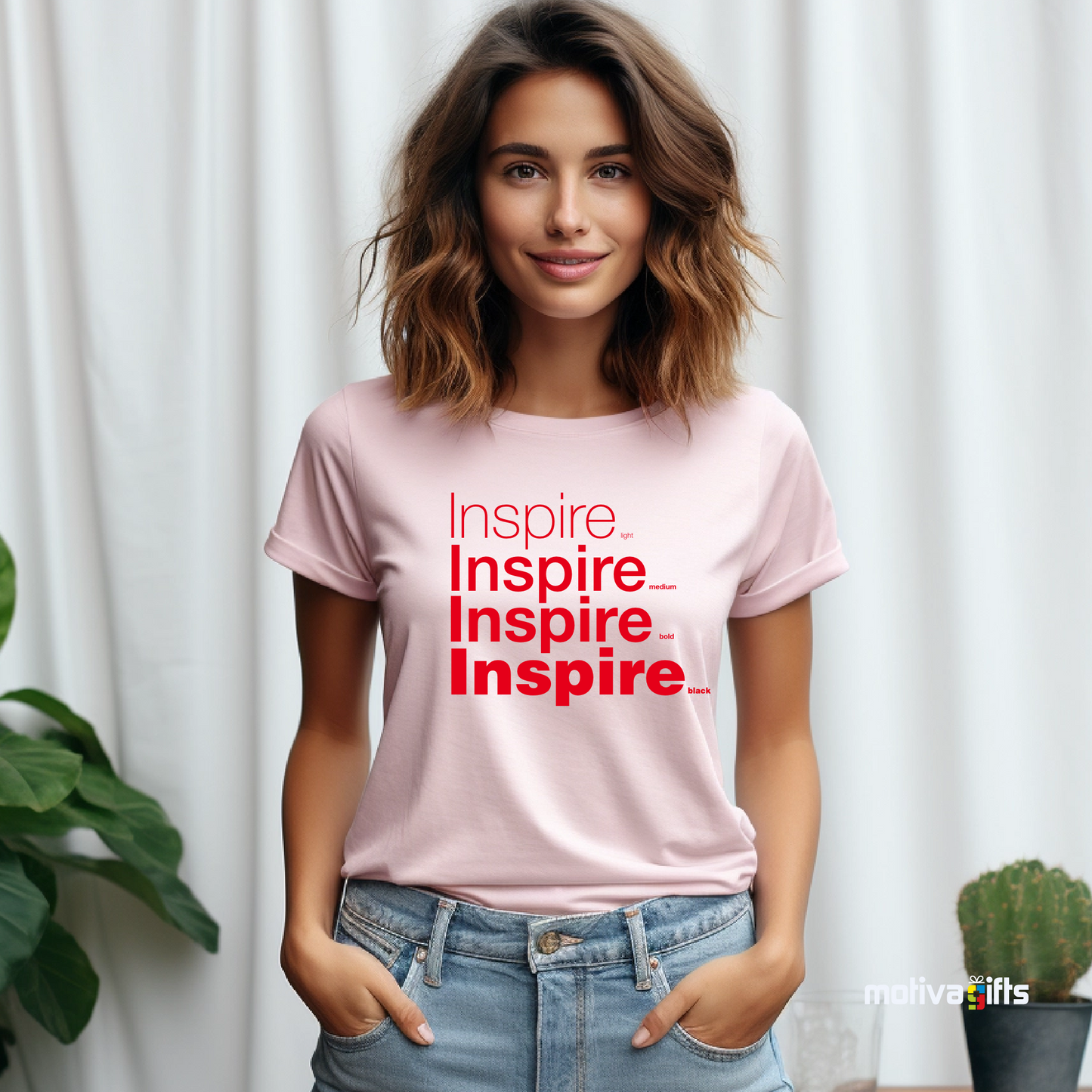 Woman using Little Pink unisex t-shirt with Inspire printed in red on the front in four lines with different font weights (light, medium, bold, black). Made of cotton and polyester, short sleeves, crewneck. By Motiva Gifts.