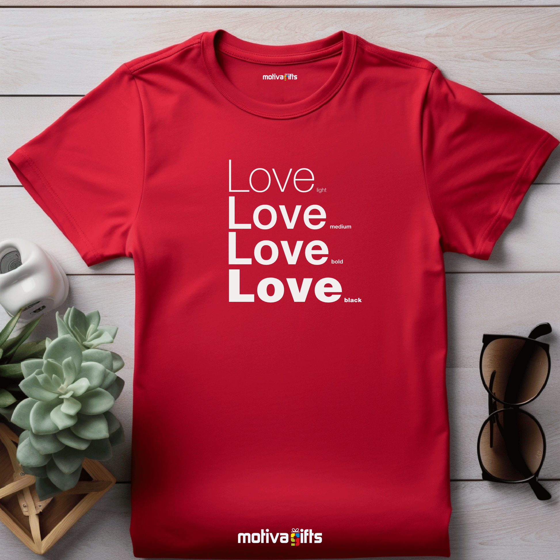 Flatlay image of a red unisex t-shirt with Love printed in white on the front in four lines with different font weights (light, medium, bold, black). Made of cotton and polyester, short sleeves, crew neck. By Motiva Gifts.