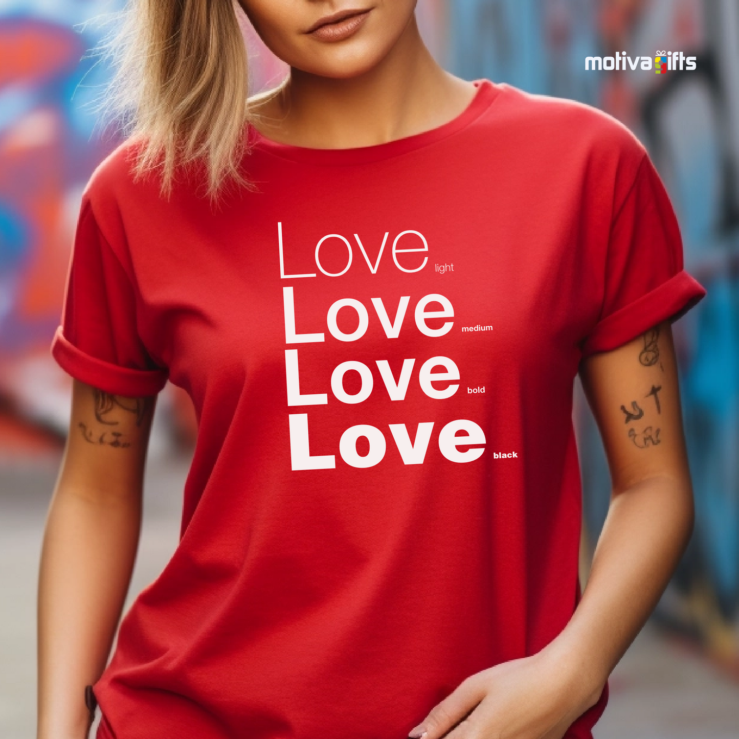 Woman using red unisex t-shirt with Love printed in white on the front in four lines with different font weights (light, medium, bold, black). Made of cotton and polyester, short sleeves, crew neck. By Motiva Gifts.