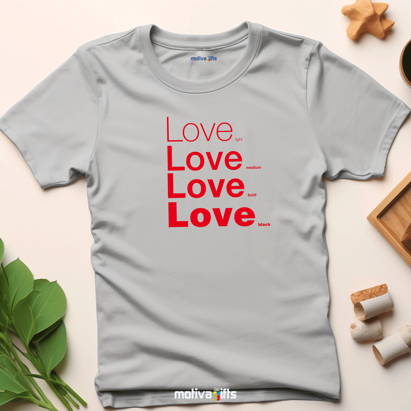 Flatlay image of a Sport Gray unisex t-shirt with Love printed in red on the front in four lines with different font weights (light, medium, bold, black). Made of cotton and polyester, short sleeves, crew neck. By Motiva Gifts.