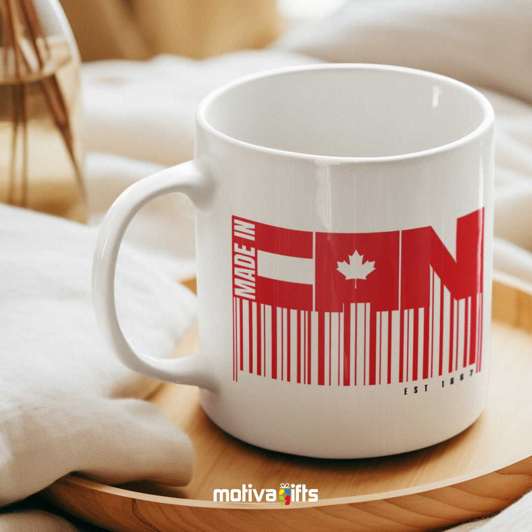 Made in CAN reads in Red bold letters on a white 11 oz ceramic mug, featuring a wood table.