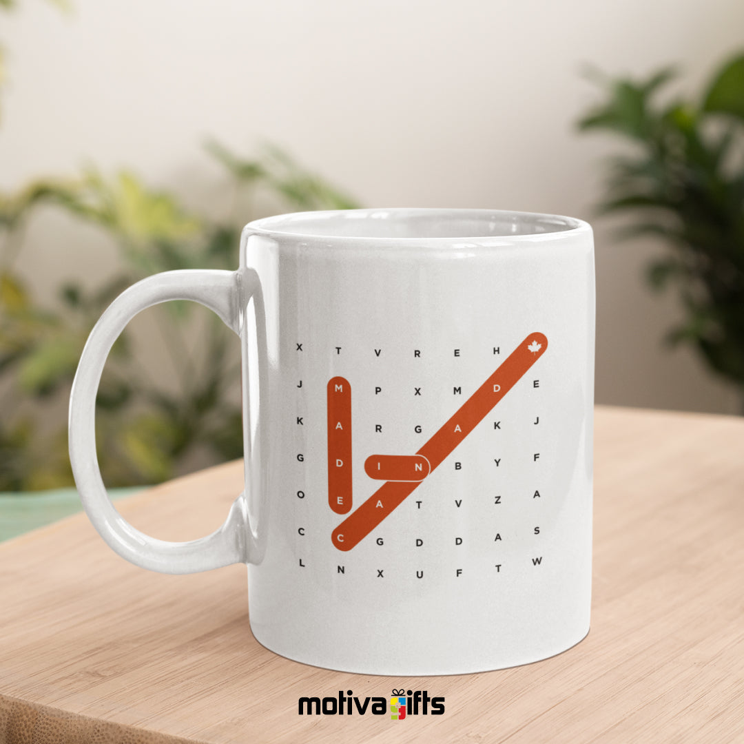 Made in Canada Crosswords reads in black/Red bold letters on a white 11 oz ceramic mug, featuring a wood table.