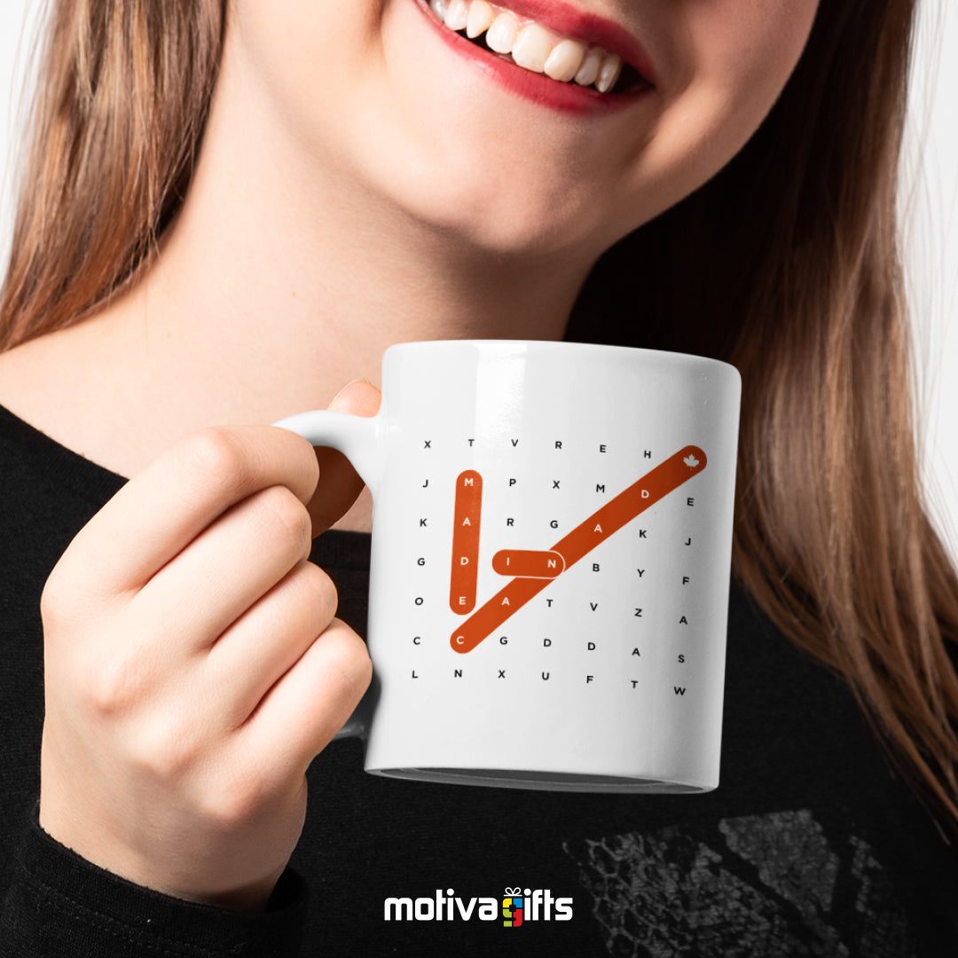 A woman holding a white 11oz ceramic mug that reads in black/red bold Made in Canada Crosswords art printed on both sides