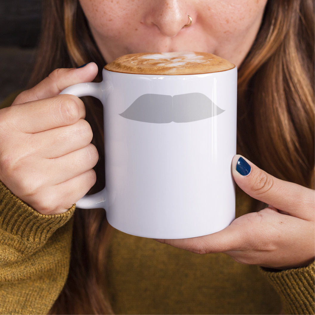 Woman holding a white ceramic mug with a drawing of Mahatma Gandhi’s mustache