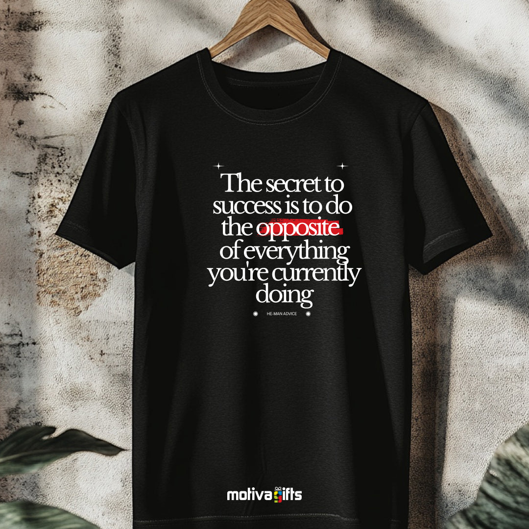 A hanging black T-shirt featuring bold white typography that reads The secret to success is to do the opposite of everything you’re currently doing