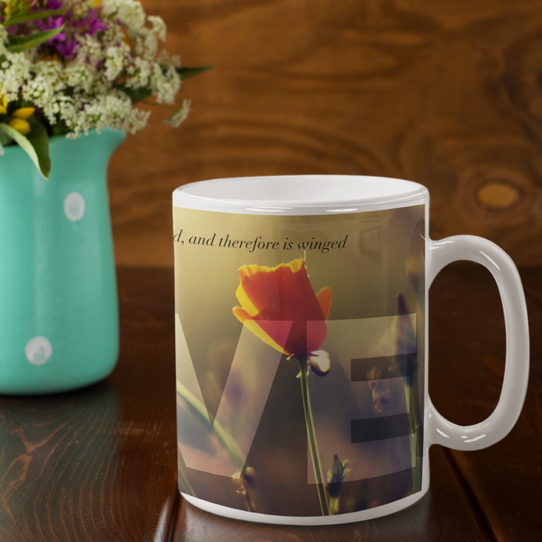 white ceramic mug with a wraparound design displaying the word ‘Love’ above a quote by William Shakespeare: ‘Love looks not with the eyes but with the mind, and therefore is winged Cupid painted blind’, featuring a table and a vase of flower