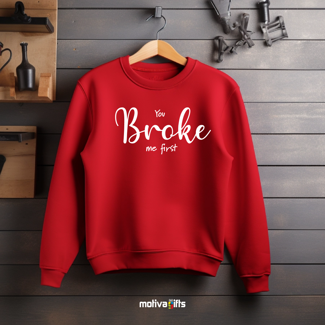 A hanging red sweatshirt featuring bold white typography that reads You Broke Me First