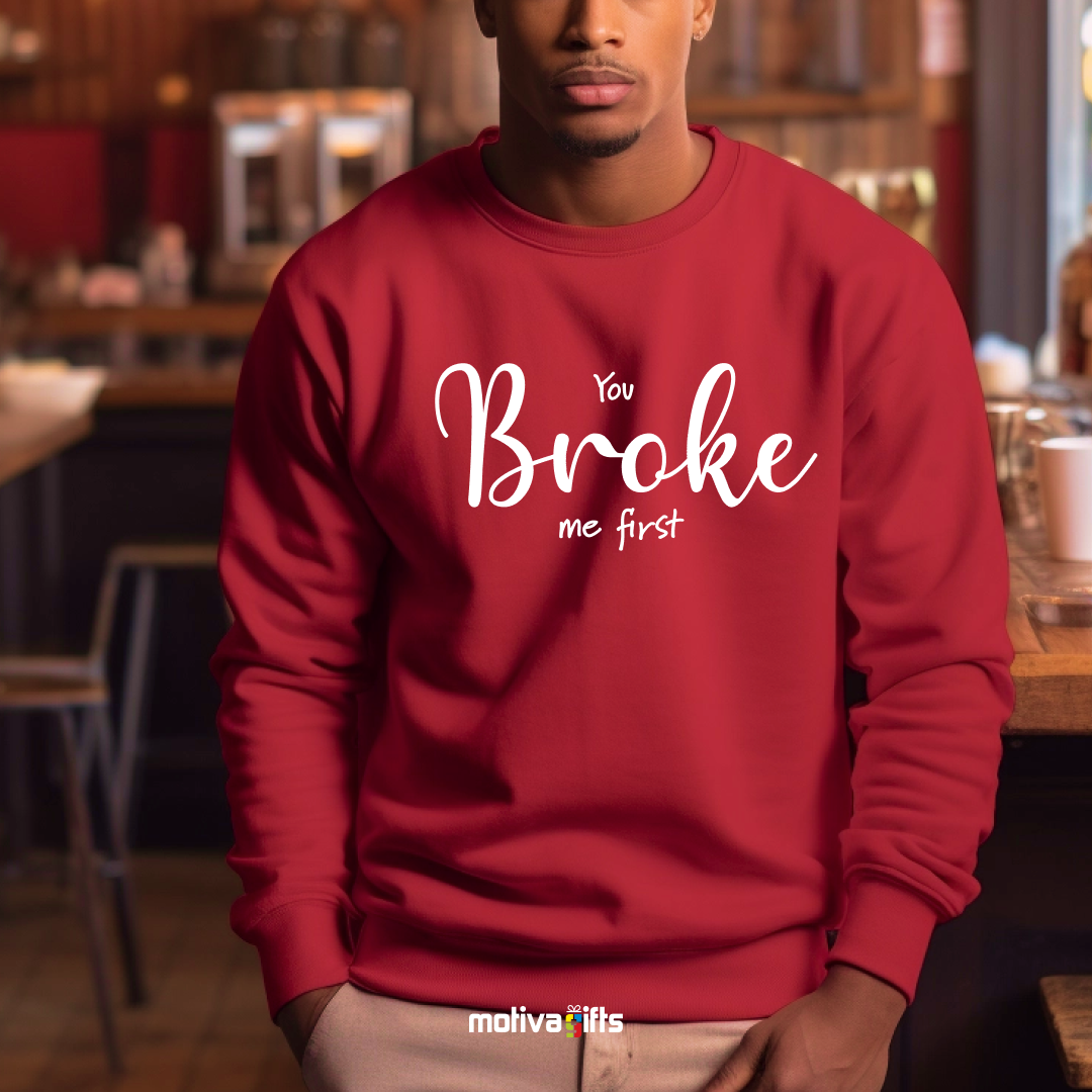 A man wearing a red crewneck sweatshirt featuring white typography that reads You Broke Me First