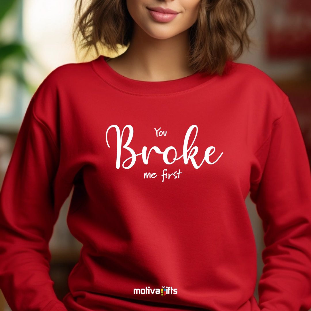 A woman wearing a red crewneck sweatshirt featuring white typography that reads You Broke Me First