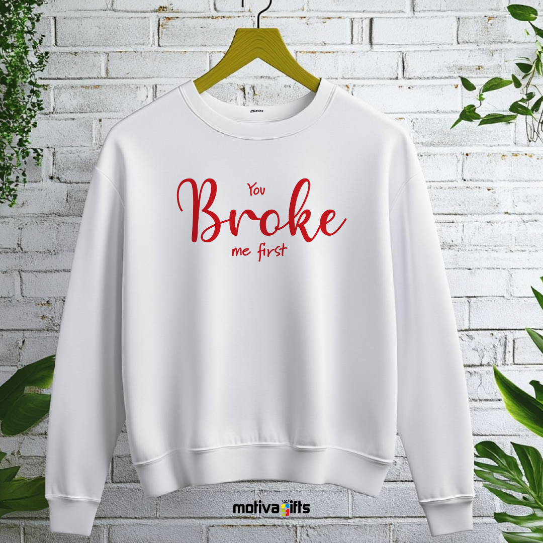 A hanging white sweatshirt featuring bold red typography that reads You Broke Me First